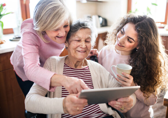 Trois femmes d'âge différents souriantes, utilisant une tablette